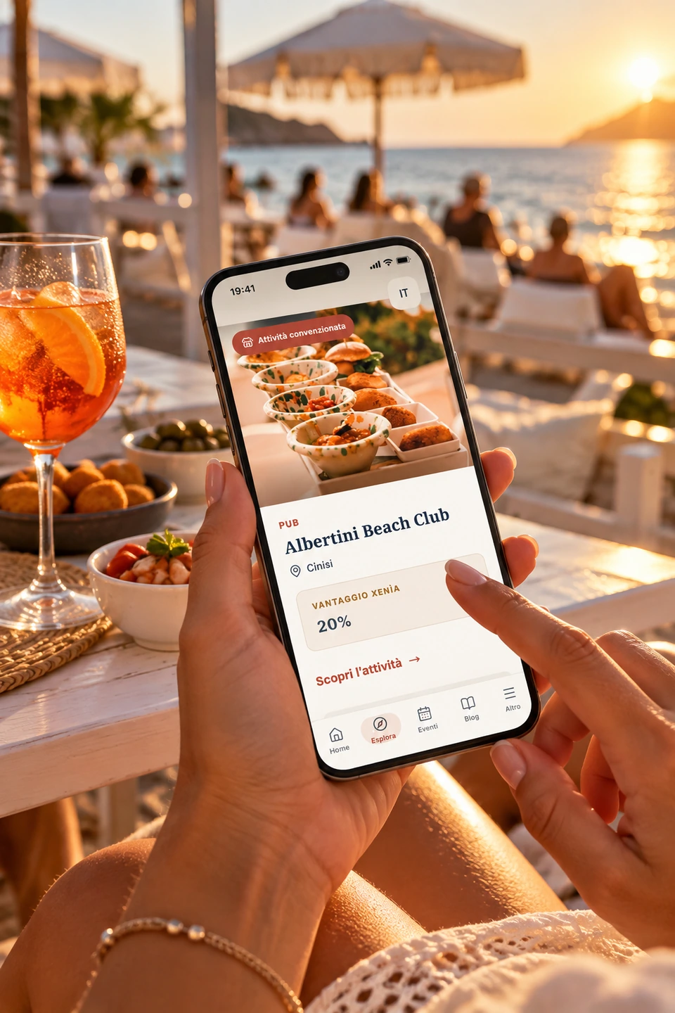 Una persona consulta Albertini Beach Club su Xenia Hub, usando lo smartphone in un locale sul mare al tramonto